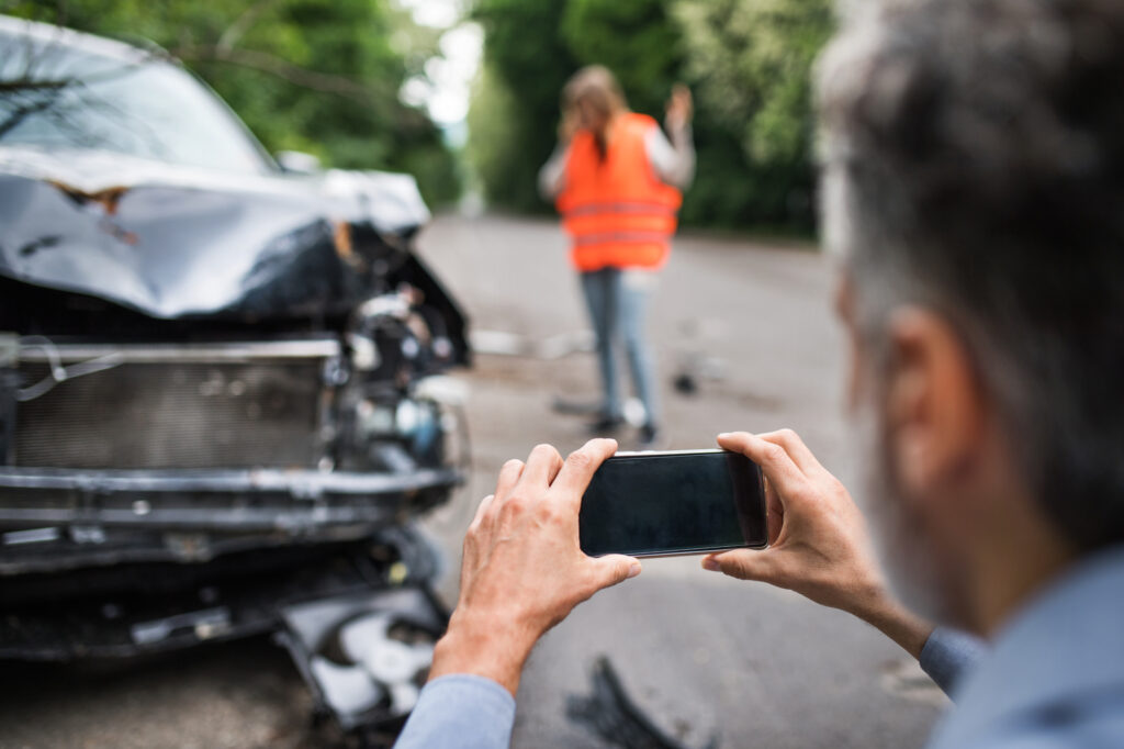 2 Myths Regarding Car Accidents - Unrecognizable man taking pictures of a broken car after an accident.